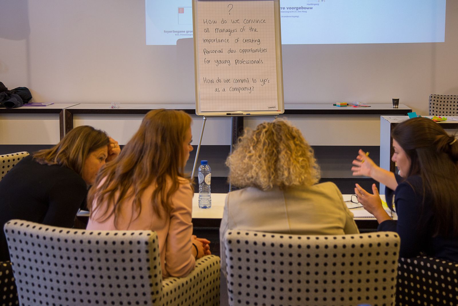 4 vrouwen voeren een energiek gesprek voor een bord met 2 vraagstukken erop