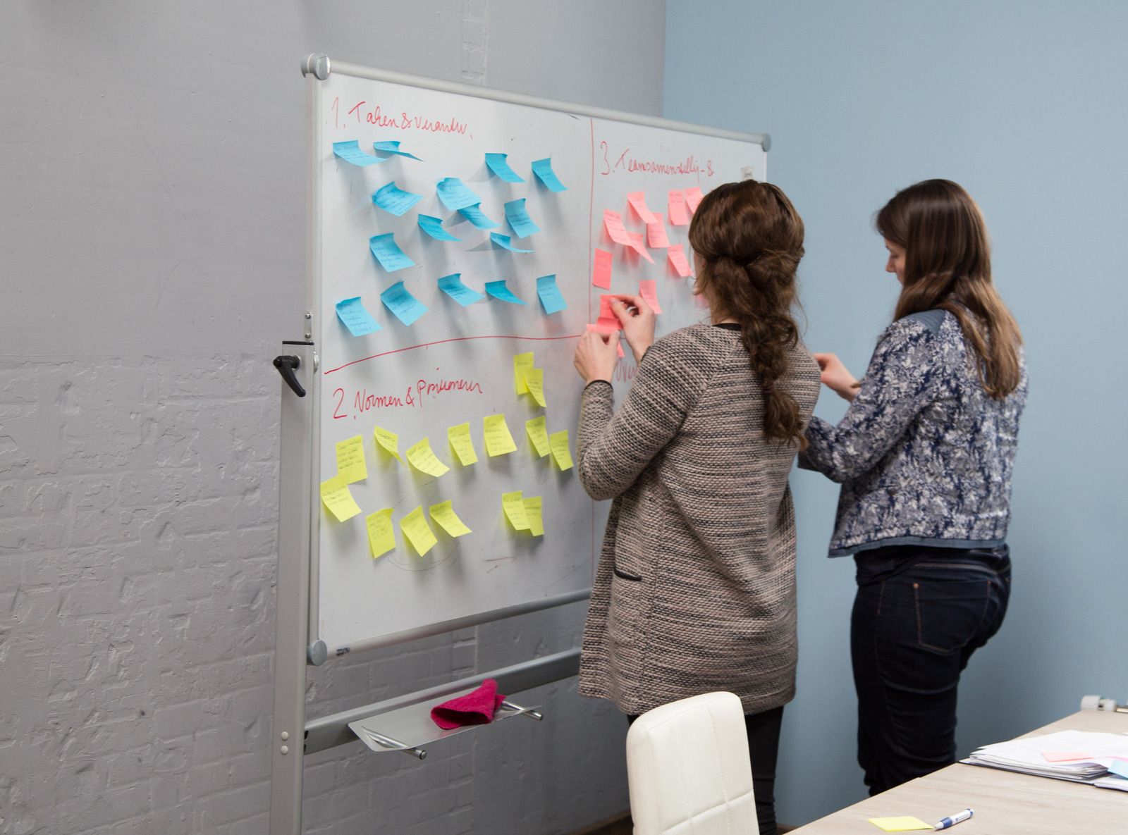 2 dames staan bij bord vol post-its en maken een indeling